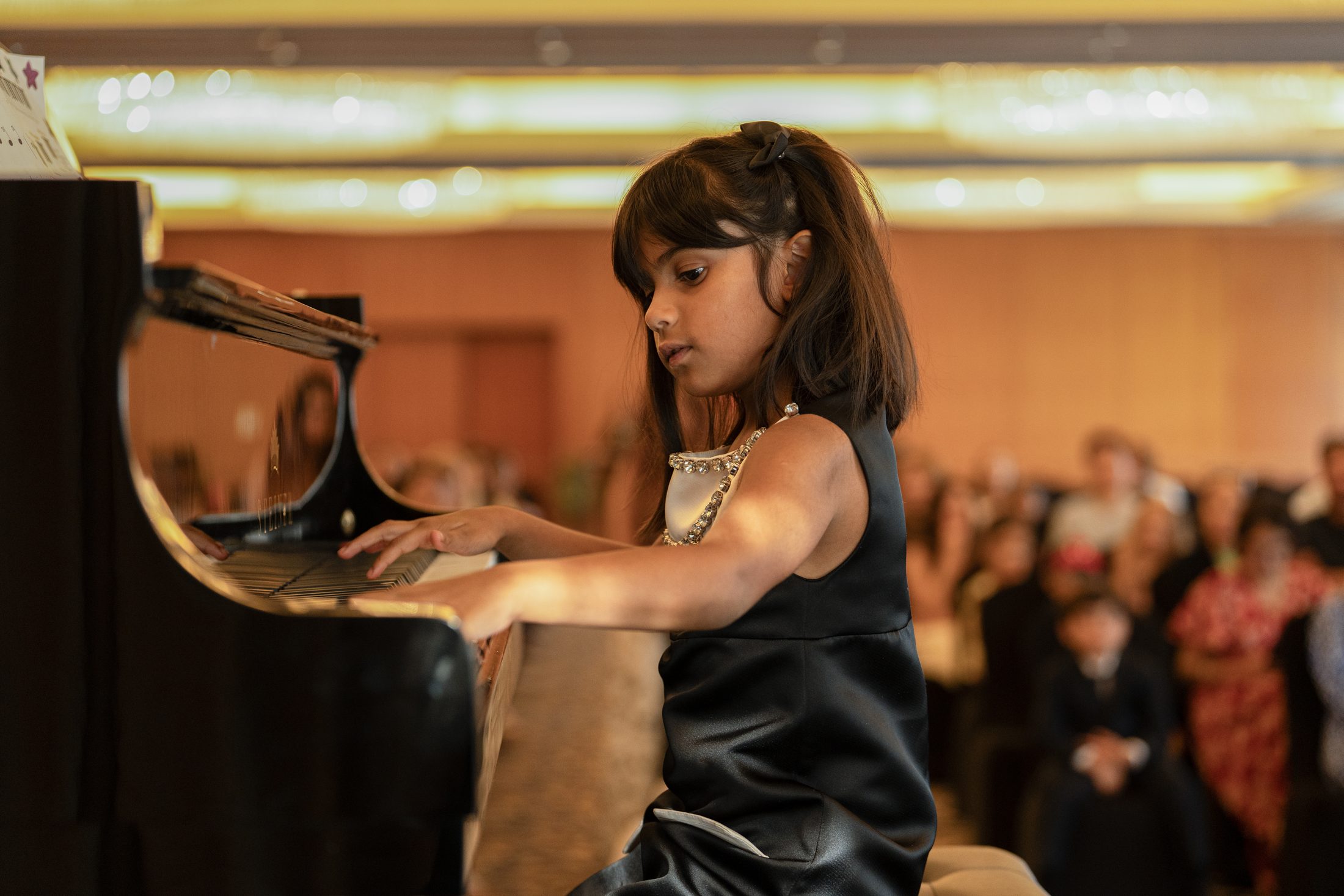 A young pianist performing on a grand piano at an MJ Strings recital in Dubai